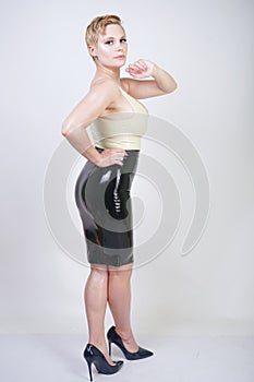 Hot short hair blonde girl with curvy body wearing latex rubber dress on white studio background
