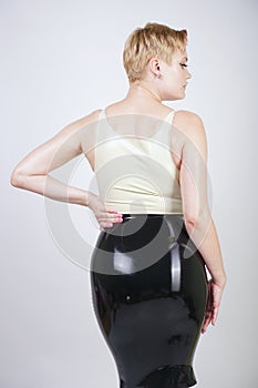 Hot short hair blonde girl with curvy body wearing latex rubber dress on white studio background