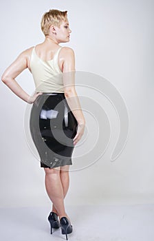 Hot short hair blonde girl with curvy body wearing latex rubber dress on white studio background