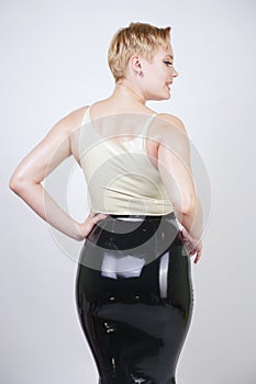 Hot short hair blonde girl with curvy body wearing latex rubber dress on white studio background