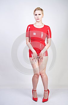 Hot short hair blonde girl with curvy body wearing latex rubber dress on white studio background