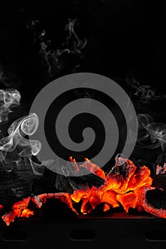 Hot smouldering charcoals on bbq grill on black background with white smoke