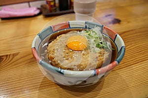 Hot soba with deep fried egg with onion in Japanese bowl on timber table