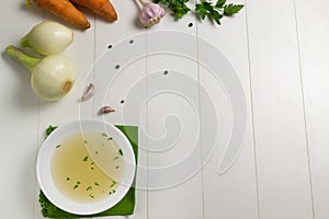 Fresh bouillon in a white plate with finely chopped herbs on a green napkin with ingredients on a white background. photo