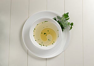 Fresh bouillon in a white plate with finely chopped herbs on  a white background.  Copy space. photo