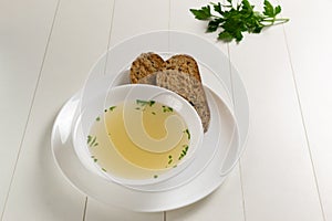 Fresh bouillon in a white plate with herbs and croutons of grain bread on a white background. photo
