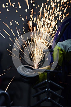 Hot sparks flying while worker is grinding steel pipe with a circular saw.