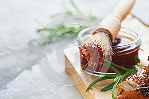 Hot and spicy barbecue sauce in jar bowl with basting brush on old stone gray background. Flat lay composition. American food conc