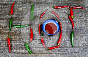 Hot spicy food symbol concept: Close up of blue bowl with chili sauce on wood table with green red Chillies forming the word hot