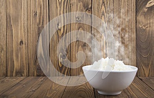 Hot Steamed Rice in a White Bowl with White Vapor on wooden background