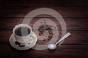 Hot steaming coffee in a cup and saucer on a table with sprinkled coffee beans.