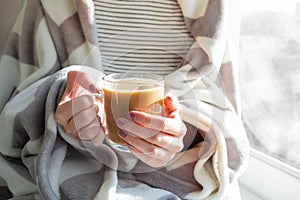 Hot steaming drink in woman`s hands. Female covered in throw bla