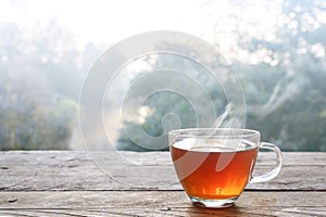 Hot steaming tea in a glass cup on a rustic wooden outdoor table on a cold foggy winter day, copy space, selected focus, narrow