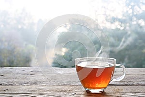 Hot steaming tea in a glass cup on a rustic wooden outdoor table on a cold foggy winter day, copy space, selected focus, narrow photo