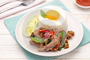 Hot stir-fried pork slices with holy basil leaves served with cooked rice topped with a fried egg