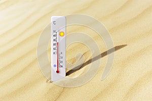 Hot summer day. Celsius scale thermometer in the sand.