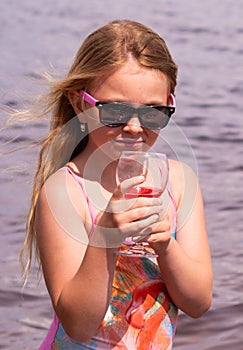 On a hot summer day, a child is relaxing on the lake. A girl on the beach. The girl drinks delicious fresh juice.