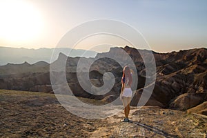 Hot sun is shining down before sunset to desert surreal landscape with beautiful travel girl standing from back, Death Valley USA