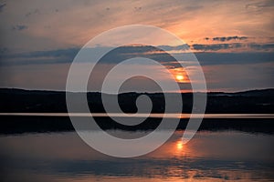 Hot sunset above the forest. Refelctions of red clouds in the water of the lake. bright colors at the end of a summer day