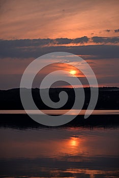 Hot sunset above the forest. Refelctions of red clouds in the water of the lake. bright colors at the end of a summer day