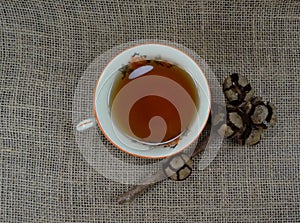 Hot tea cup white porselain with decoration on burlap and at black wooden background