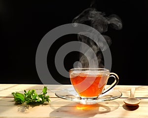 Hot tea in glass cup with steam and lemon .tea leaves and mint herb on wood background