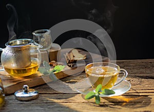 Hot tea in glass teapot and cup with steam on wood background