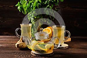 Hot tea with lemon, orange, ginger and mint on wooden table in the morning