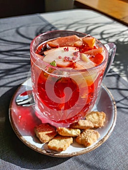 Hot tea mug with grenadine and fruits next to cookies on a table in a cafe in bright sunlight