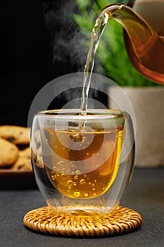 hot tea pouring from teapot into glass cup on table