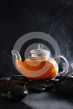 Hot tea with sea buckthorn in a transparent glass teapot. A healthy drink. Natural vitamin C. Photo on a black