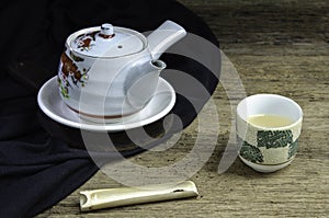 hot tea from a teapot in cup,  teas in spoon bamboo on the black cloth on the old wood table a black background Right side copy