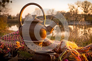 Hot teapot at autumn sunset on riverbank