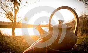 Hot teapot at autumn sunset on riverbank