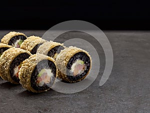 Hot tempura black rice sushi roll with salmon, tuna, rockfish, avocado and cream cheese inside roll on dark background