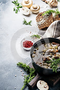 Hot thick mushroom soup with beef, spices and wholegrain barley, meat broth. With black bread, in metal pan, top view, flat lay,