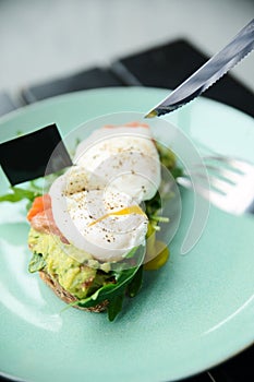 Close-up poached egg with yolk on toast with avocado and salad