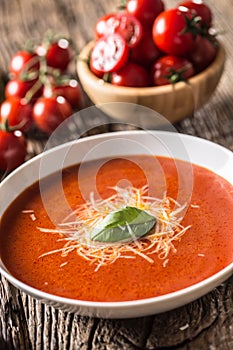 Hot tomato soup parmesan cheese and basil leave on old oal table