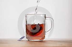 Hot water is poured into a glass mug with a tea bag. Frontal view