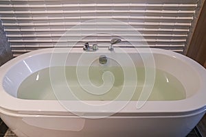 Hot water in white ceramic bathtub in hotel bedroom