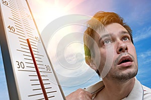 Hot weather concept. Young man is sweating. Thermometer is showing high temperature. Sun in background