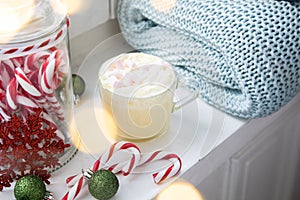 Hot white chocolate with whipped cream and marshmallows on windowsill with cosy wool rug blanket and book at Christmas X-Mas