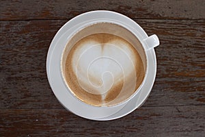 Hot white cup of coffee with heart shape on wood table from top view