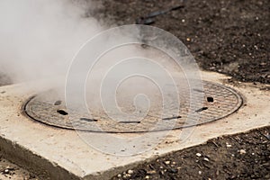 Hot white steam coming out of metal manhole or metal hatch