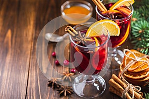 Hot wine drink with spices and fruits in a tall glass and branches of a Christmas tree on a wooden background
