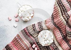 Hot winter drink with cocoa, chocolate and marshmallows in cups on gray background with knitted warm sweater, top view