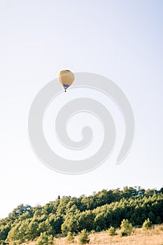 Hot yellow air balloon high in the sky, flying in beautiful green summer field at sunset