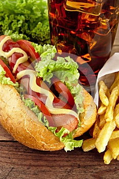 Hotdog with french fries with glass of cola on wooden plank