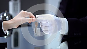 Hotel administrator hand in glove giving lady key on chain, vip service, luxury
