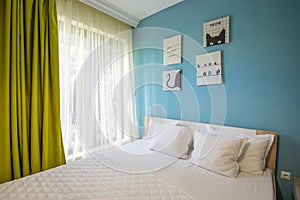 Hotel bedroom with blue walls, white sheers, pillowcases and sheets. Green curtains